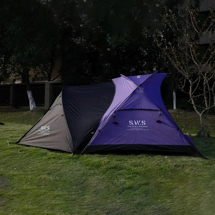 Backpacking tent with stove jack in black and blue, pitched on grass with trees in the background. A durable and spacious shelter designed for warmth and weather protection.