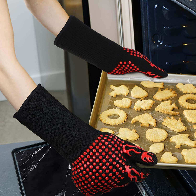 Person wearing black and red heat resistant BBQ gloves removing a tray of freshly baked cookies from the oven.