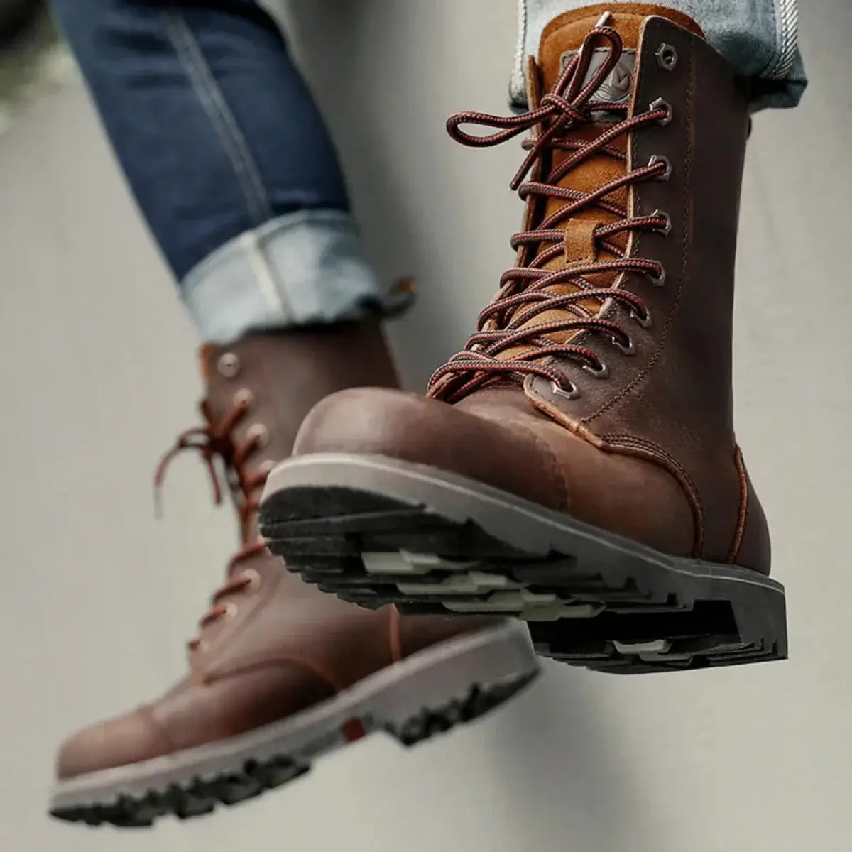 Close-up of brown leather boots with red laces, dark brown toe cap, and thick sole, worn with blue jeans.