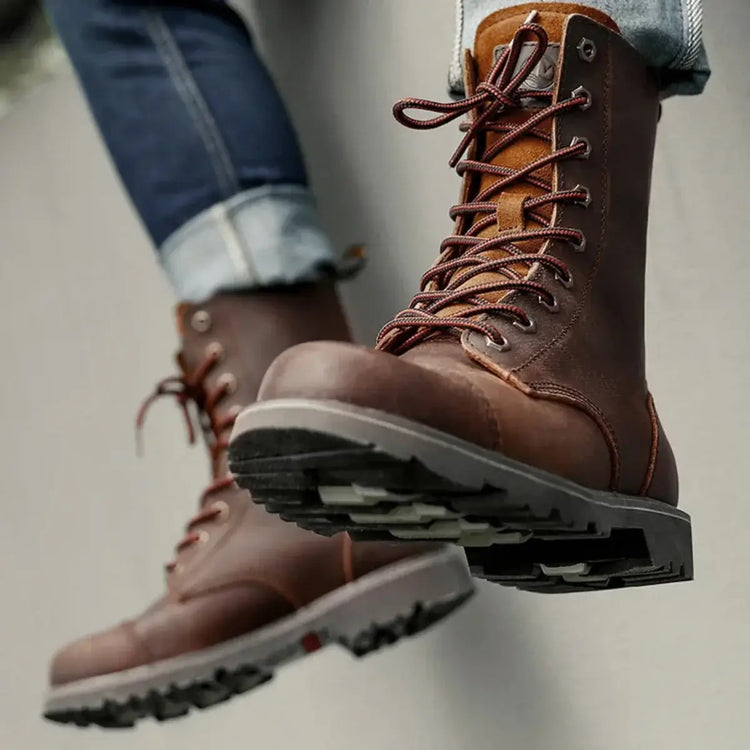 Close-up of brown leather boots with red laces, dark brown toe cap, and thick sole, worn with blue jeans.
