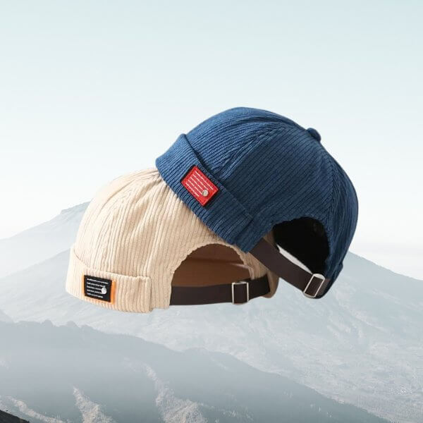 Blue and beige corduroy brimless hats showcasing adjustable straps and high-quality craftsmanship against a mountain background