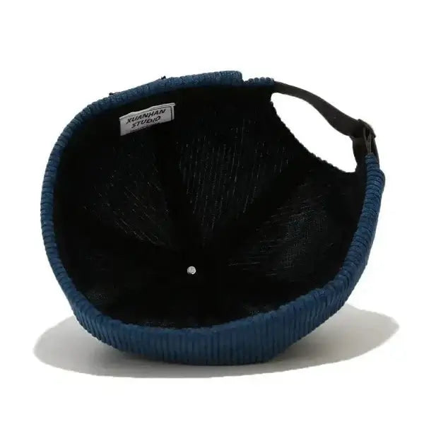 Blue corduroy brimless skull cap with an adjustable strap, showcasing the interior fabric and label.