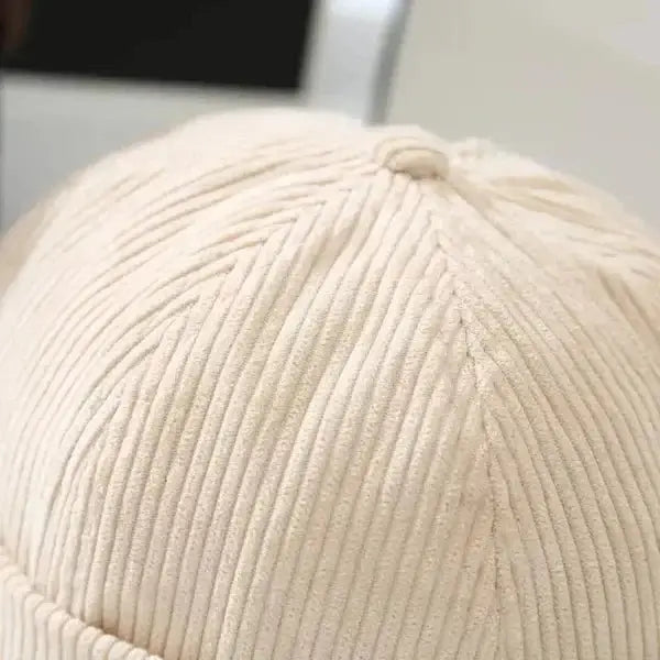 Close-up of a beige corduroy brimless hat showing detailed fabric texture.