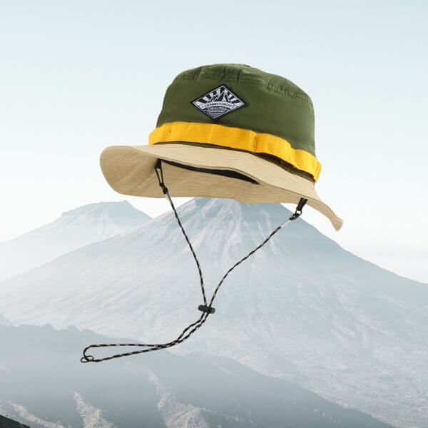 Green and yellow wide brim fishing bucket hat with chin strap against mountain background