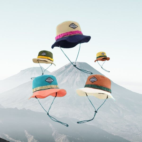 Colorful wide brim bucket hats with chin straps floating in front of a mountain scenery.