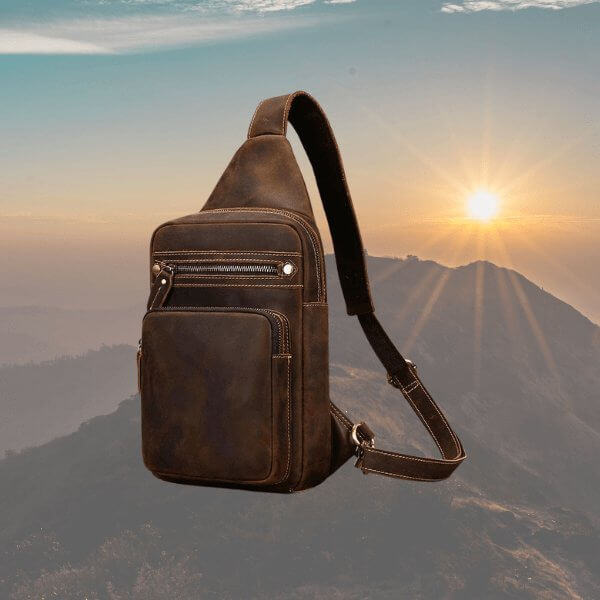 Soft leather crossbody bag with carrying strap, zipper opening, two external pockets, sunset and mountains background.