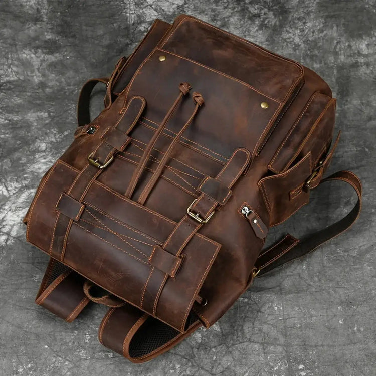Front view of a brown leather backpack with buckle straps and a drawstring closure.