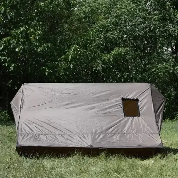 Lightweight hot tent for camping set up in grassy area surrounded by trees.