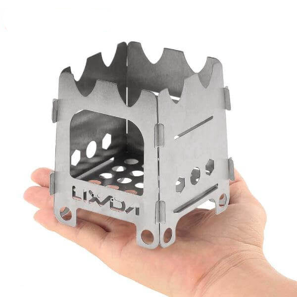 Titanium ultralight folding wood stove for camping shown in a hand, highlighting its small and portable design.