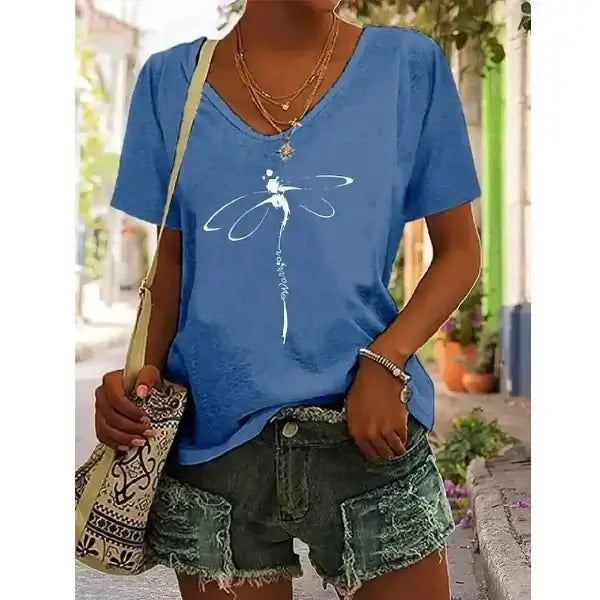 Woman wearing blue V-neck graphic tee with dragonfly design, paired with denim shorts and a boho bag, perfect for effortless summer style.
