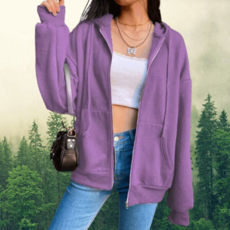 A woman wearing a purple long-sleeved hoodie with an oversized hood and an adjustable collar stands against a forest background.