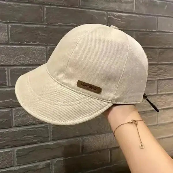 Cream-colored handmade wide brim cotton cap for women held by a hand, displayed against a brick background.