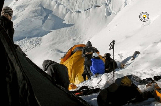 Snow camping enthusiasts setting up a tent on a snowy mountain slope, surrounded by gear and winter landscape.