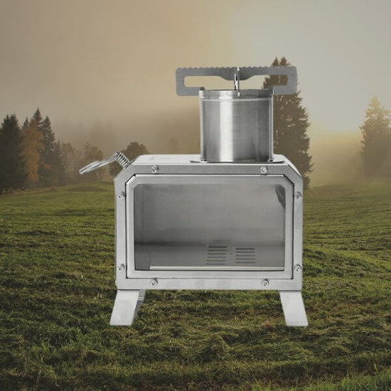 Portable stainless steel camping wood stove on grass field with trees in background