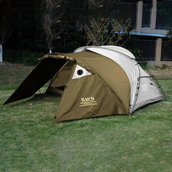 Backpacking tent with stove jack in forest green, shown on green grass with a backdrop of trees and fence. with good insulation and space for extended hiking and camping trips.