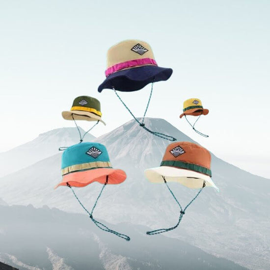 Colorful wide brim bucket hats with chin straps floating in front of a mountain scenery.