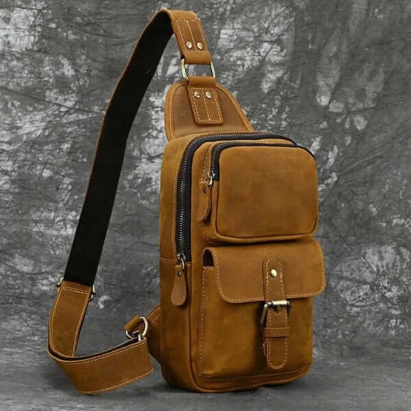 Crossbody bag designer, light brown, brushed leather, carrying strap, metal buckle, top zipper opening, front and side view, gray background.