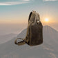 Small leather crossbody bag with a zipper, carrying strap, dark brown, in front of sunset and mountains.