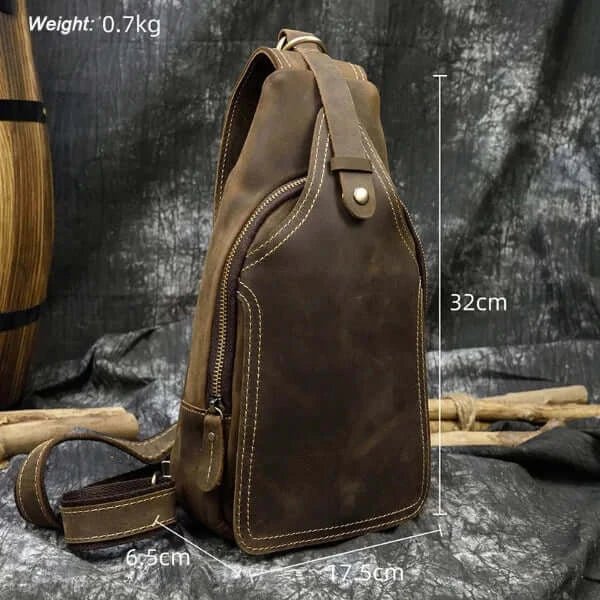 Peak design sling, dark brown leather, top zipper, pointed upper part, closing strap, front view, with measurements.