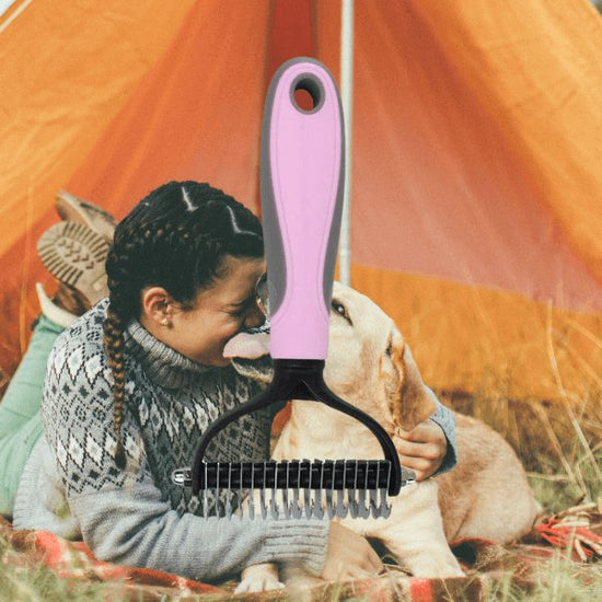 Pink dog de-shedding brush, background of a woman hugging a Labrador licking her face in a tent.