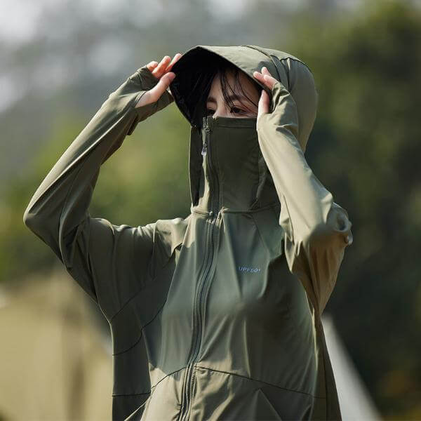 Woman wearing sun protective hooded jacket with UPF 50+ in green, shielding her face with the hood. Perfect for summer outdoor activities.