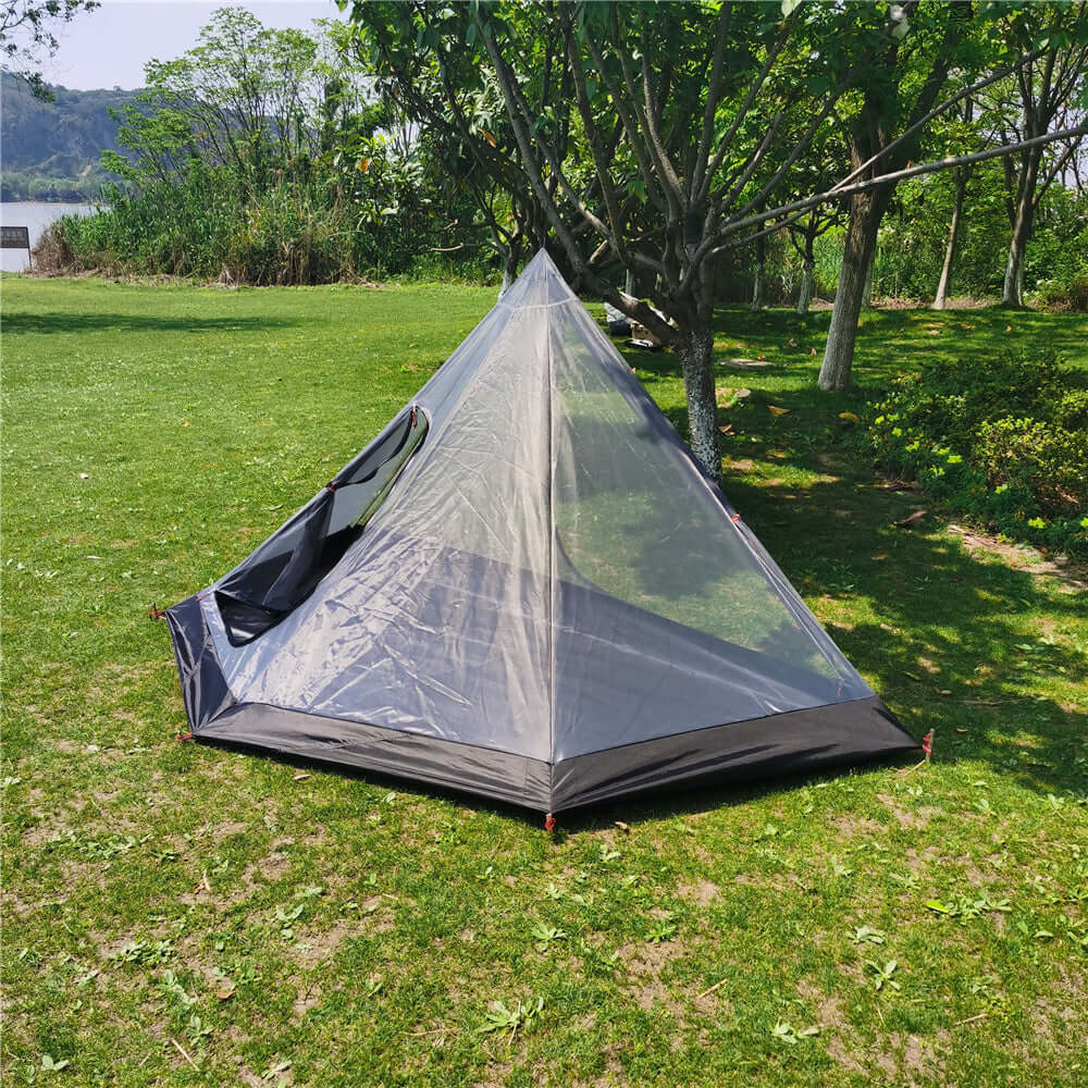 Hot tent with stove setup on grass, ideal for winter camping. Spacious and lightweight, perfect for backpacking trips.