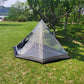 Hot tent with stove setup on grass, ideal for winter camping. Spacious and lightweight, perfect for backpacking trips.