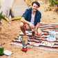 Man using portable backpacking gas stove for outdoor cooking on a camping trip next to tent and picnic setup