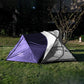 Backpacking tent with stove jack in bold purple and gray, positioned on grassy ground with trees behind. Eye-catching design built for warmth and wilderness performance.