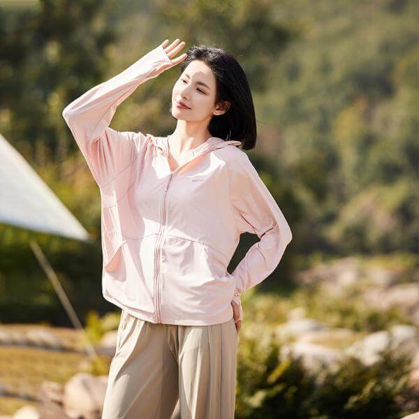 Woman wearing a sun protective pink hoodie jacket with UPF 50+ fabric, enjoying outdoor protection.