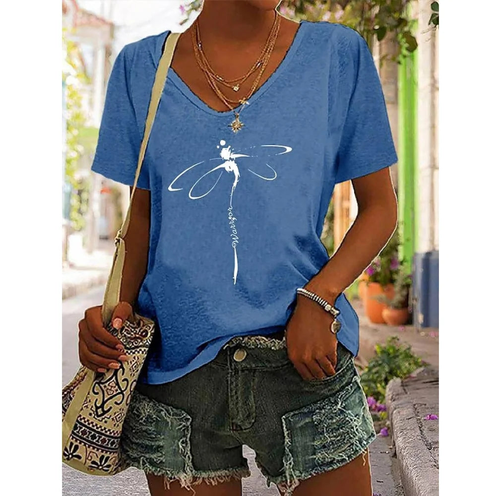 Woman wearing blue V-neck graphic tee with dragonfly design, paired with denim shorts and a boho bag, perfect for effortless summer style.