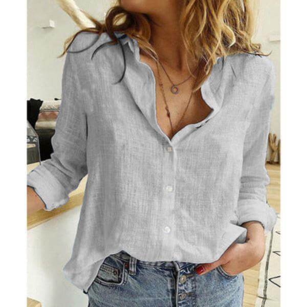 Woman wearing a light gray linen blouse with button details, showcasing casual summer style in a cozy setting.