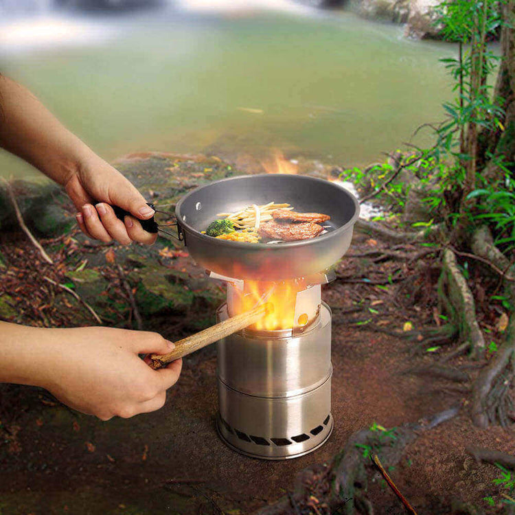 Cooking on a portable stainless steel wood burning camping stove by a river in the wilderness