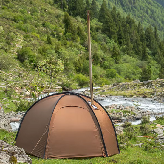 Brown camping tent set up in a natural outdoor setting with greenery and a stream.