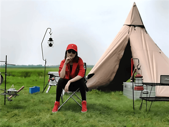 A spacious, pyramid-shaped tent, pitched on a grassy field with a woman sitting in front.