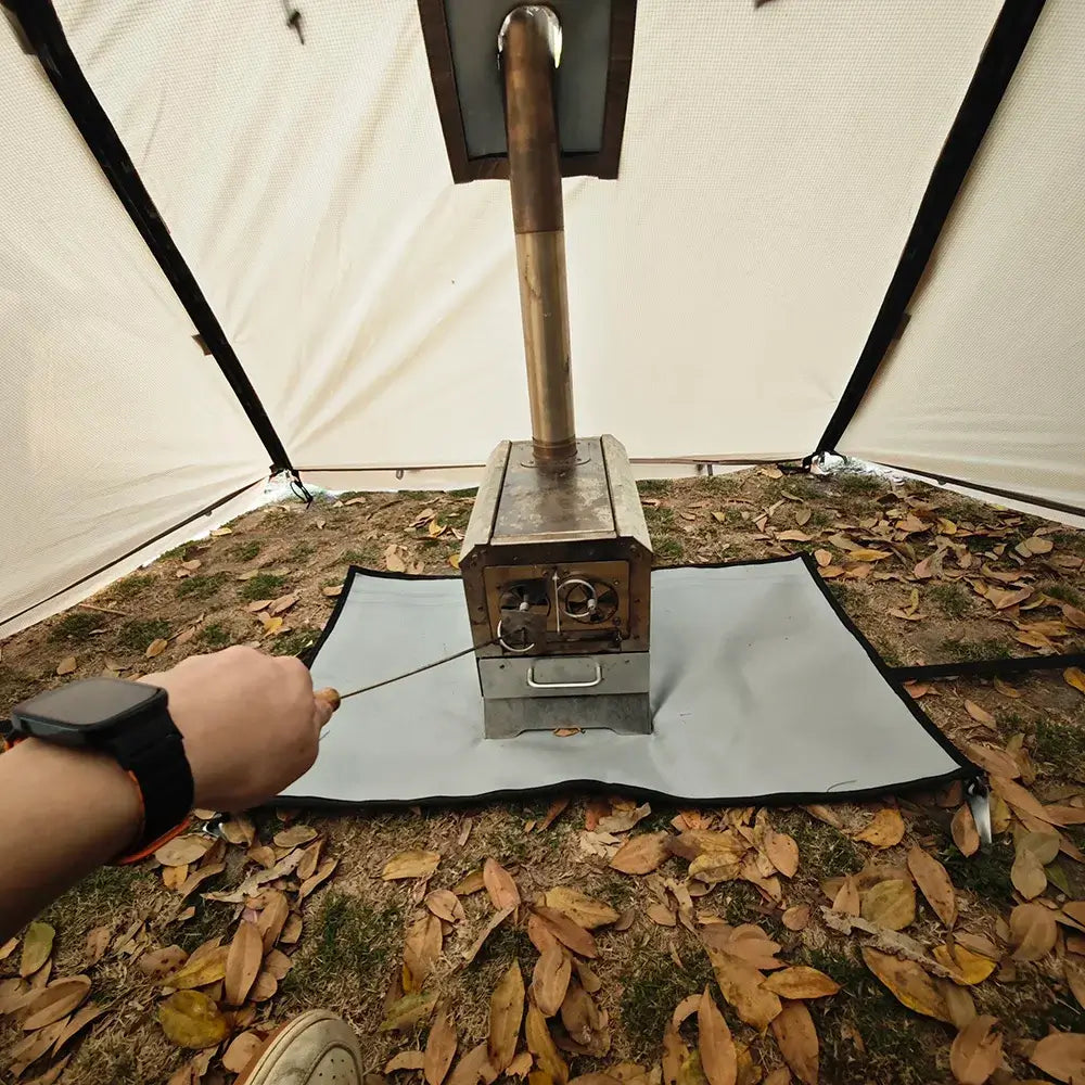 A close-up view of a wood-burning stove inside a tent, with a person&