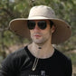 Man wearing wide brim safari hat with UPF 50+ sun protection and sunglasses outdoors.