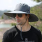 Man wearing a gray wide brim bucket hat with a chin strap, ideal for sun protection and outdoor activities like fishing and hiking.