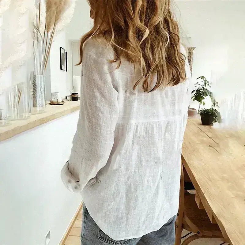 Woman wearing a white cotton linen shirt with roll-up long sleeves and a V-neck lapel collar, standing in a cozy, minimalist room.