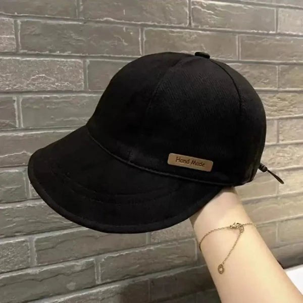 Black handmade wide brim cap for women with adjustable strap against brick wall