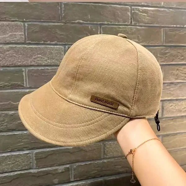 Beige cotton baseball cap held by hand against brick background