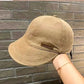 Beige cotton baseball cap held by hand against brick background