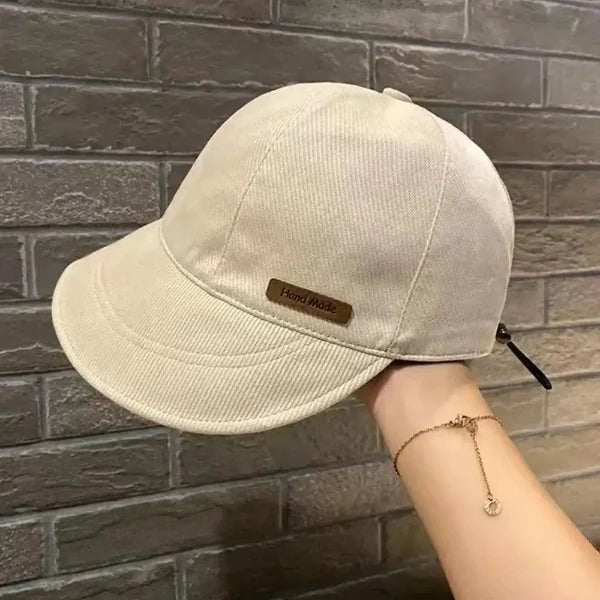 Cream-colored handmade wide brim cotton cap for women held by a hand, displayed against a brick background.