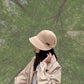 Beige handmade cotton bucket hat with a wide brim held against a brick wall background.